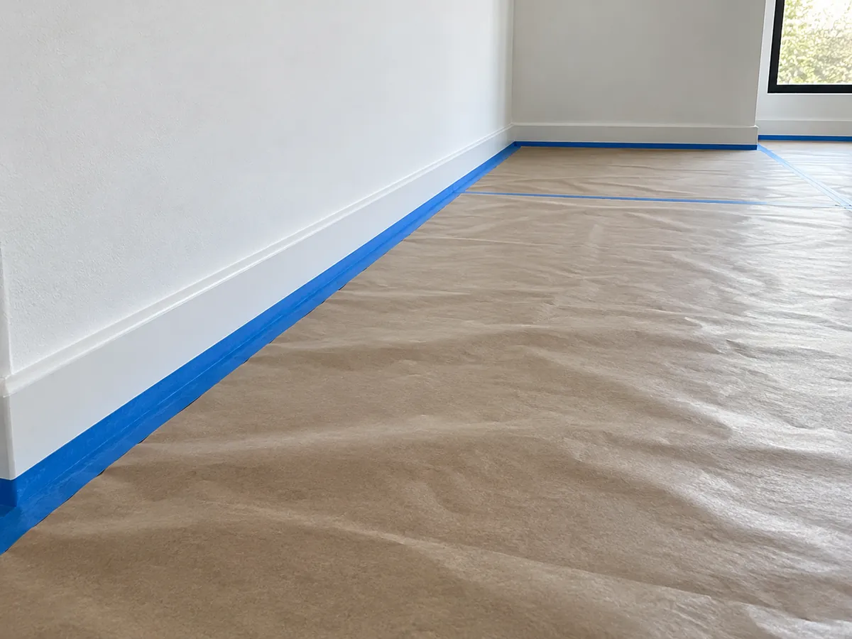 Vloer afgedekt met papier en plint afgeplakt met blauwe tape